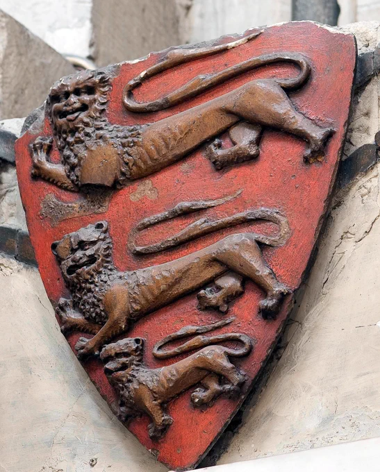 A carved red shield, decorated with the figures of three lions, on an ancient stone wall in Westminster Abbey