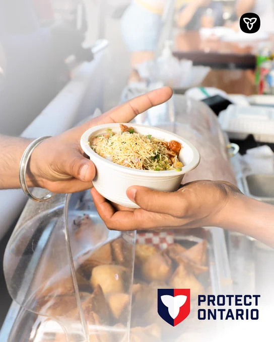 Hands hold a bowl of noodle‑style street food topped with sauce and herbs at an outdoor festival food stall, with fried snacks visible below. The Protect Ontario logo appears in the corner.