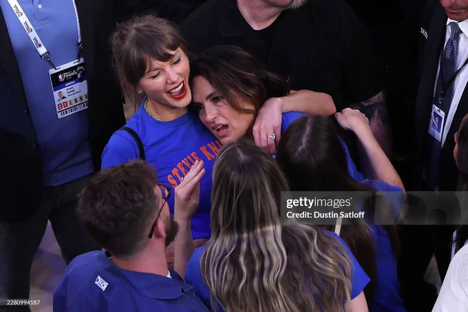 Mariska Hargitay looks distressed while a smiling Taylor Swift cradles her in a celebratory hug. This is a photo after the Knicks complete the greatest comeback in NBA history.