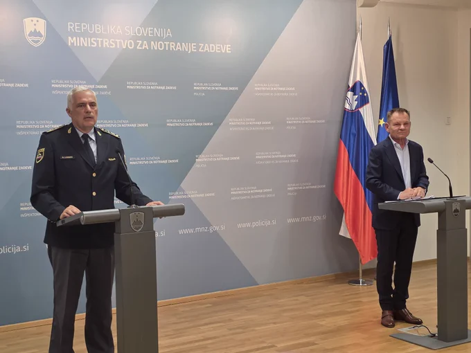 Minister za notranje zadeve in javno upravo Franci Matoz in vršilec dolžnosti generalnega direktorja policije Danijel Lorbek
Minister in vršilec dolžnosti generalnega direktorja policije stojita vsak za svojo sivo govornico, na kateri sta slovenska grba. Ozadje za njima je svetlo sive in zelene barve. Vidita se tudi zastavi Slovenije in Evropske unije na desni strani. 