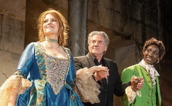 A man, flanked by two women in period dress, take a curtain call
