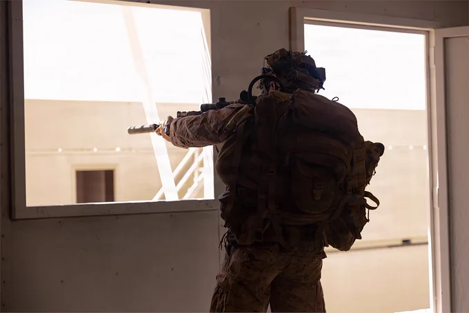 A Marine observes through a window while providing security inside a training building during an urban operations exercise.