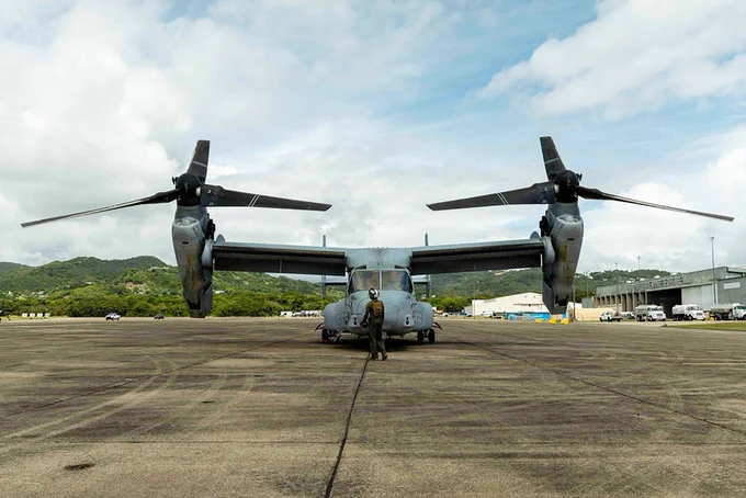 A Marine stands beneath a MV-22B Osprey as the aircraft prepares for operations on an airfield in the Caribbean.