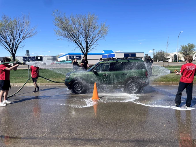 Fire Cadets spray down a green SUV with fire hoses at a charity car wash.