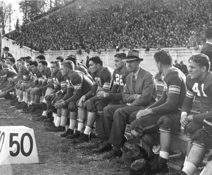 Former Duke football head coach Wallace Wade sits on a bench on the sidelines with the Blue Devil team.