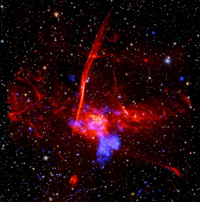This composite image of colorful, overlapping clouds, suggests to astronomers that a supernova remnant may be buried in gas near the center of our Milky Way galaxy.

Set against a backdrop packed with distant stars and other specks of light are two distinct, overlapping clouds. The larger, visually dominant cloud, is red and multifaceted. It has an irregular shape, and features patches of different textures, including pockets that resemble wispy smoke, tangles of faint red veins, and clear streaking lines. This large cloud of expanding gas represents radio data from the MeerKAT telescope in South Africa.

Overlapping with that red cloud is a cloudy blue blob representing X-ray data from NASA's Chandra X-ray Observatory and ESA's XMM-Newton. Astronomers suggest that this blue blob of X-ray emissions is the remains of a massive star destroyed by a supernova.