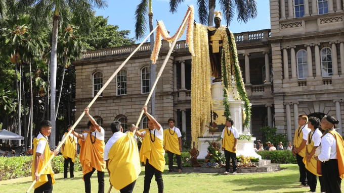 Young people place yellow flowers on a statue of King Kamehameha.