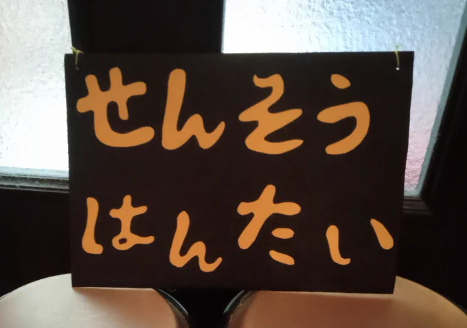 黒い背景に黄色い文字で「せんそうはんたい」と記されたプラカード