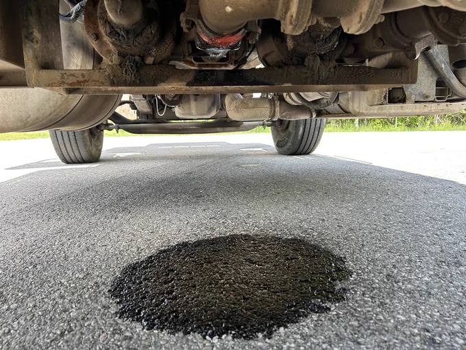 Dark circle on the pavement underneath a car where fuel was leaking.