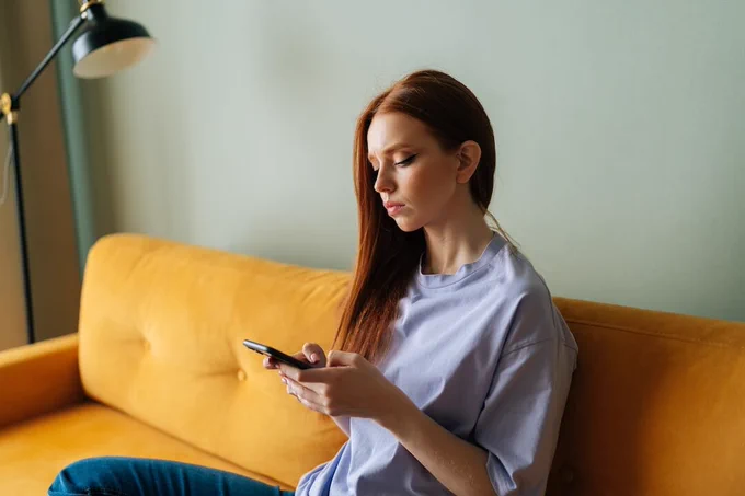 A girl using her smartphone while sitting on a sofa.