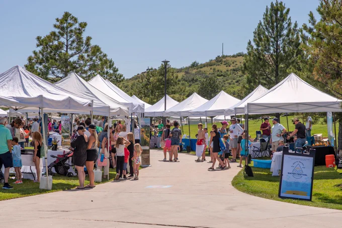 Outdoor event with people visiting several white booths lined along a concrete pathway.