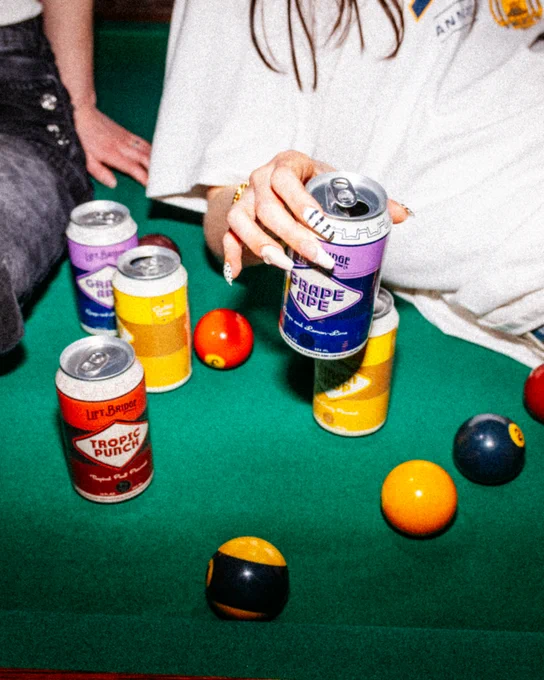 A vibrant scene with canned drinks and pool balls on a green pool table. Casual social setting with colorful elements.