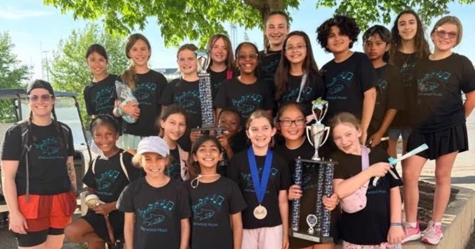 Group of girls in posing outdoors under a tree, holding trophies and medals after a competition.