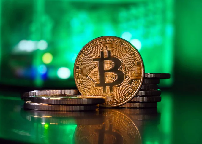 A close up of a bitcoin sitting on top of a stack of coins with a green background.