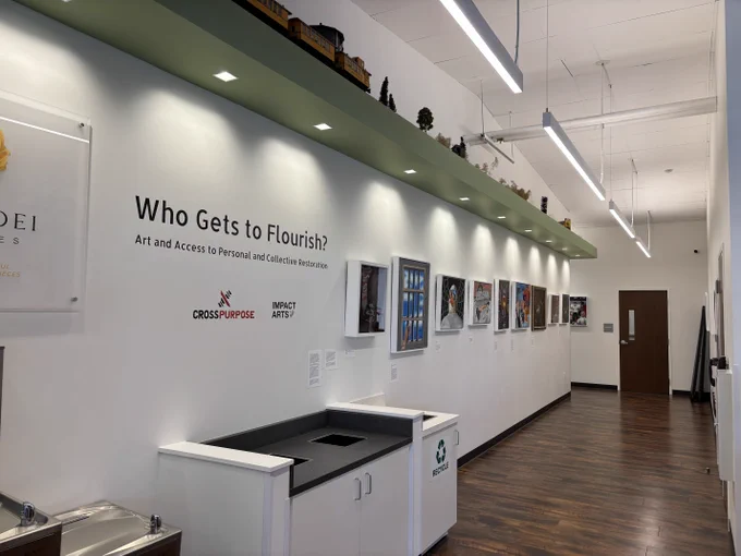Gallery hallway featuring text reading, 'Who Gets to Flourish?' with framed art pieces.