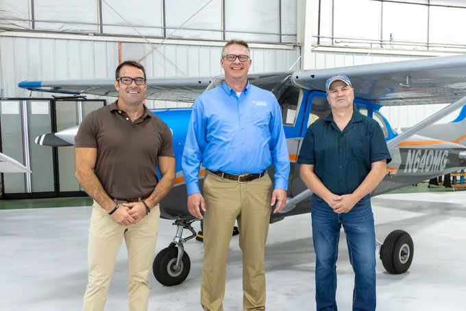 Three people are standing in front of a small airplane inside a hangar.
