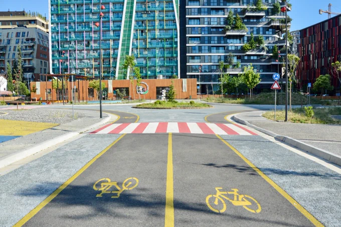 People of all ages and abilities ride bicycles along protected infrastructure lined with buildings, trees, lighting, and signage in.central Tirana.
