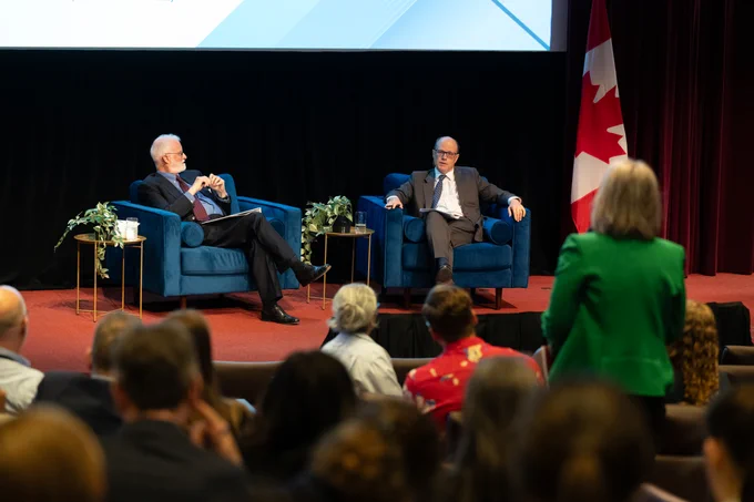 Ambassador Robert Fowler and Deputy Minister David Angell sit on stage during the event as an employee asks a question from the audience.