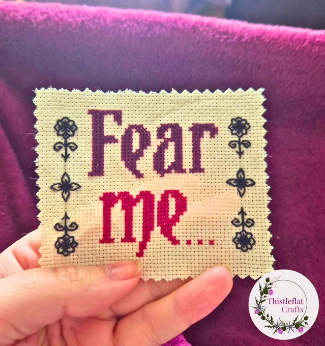 Small 3 inch cross stitch that says 'Fear me in purple and dark red stitching with a blackwork flower border