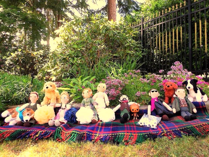 Crochet dolls l-r: Anna Strong-Hewlett, Peggy Shippen-Simcoe, Mary Woodhull, Elizabeth Woodhull-Andre, Robert Rogers with Funko-Pop Pinocchio, Owen Harper & Hermann Gottlieb sitting on a tartan blanket   toy dogs: Toby, Garrick, Ruadh & Tweed. Garden in background. 