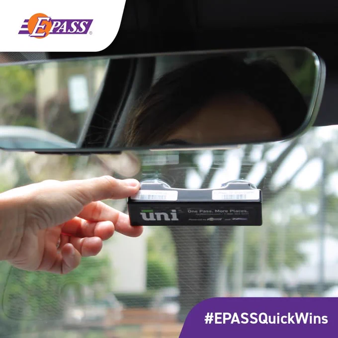 A person is placing a black E-PASS Uni transponder on a car windshield. The rearview mirror and blurred outdoor greenery are visible. The image features the E-PASS brand logo and the hashtag #EPASSQuickWins in the corners.