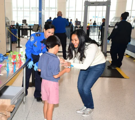 Photo shows a TSA officer assisting a child and their parent at the checkpoint