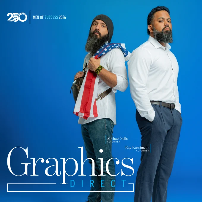 Two men stand confidently against a blue background, representing the 'Men of Success 2026' for Graphics Direct. One wears casual attire with an American flag pattern, the other is more formal.