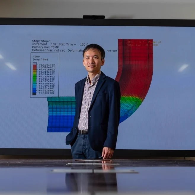 Tatsuya Sakurahara standing at the end of a table with a multi-colored risk-assessment diagram behind him