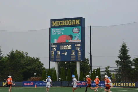 Michigan lacrosse scoreboard showing a close game with 1 minute left in the third period between teams in orange and white uniforms.