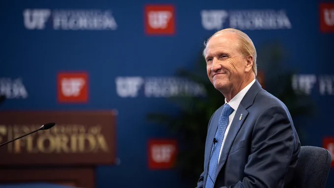 Doctor Stuart R. Bell smiling in front of a backdrop patterned with the University of Florida logo and monogram.