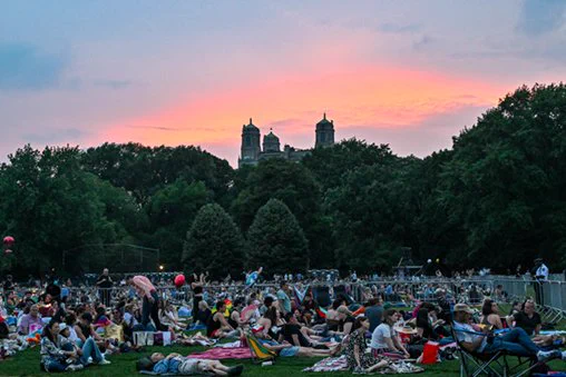 A sunset overlooking a lawn of people laying on picnic blankets in a park