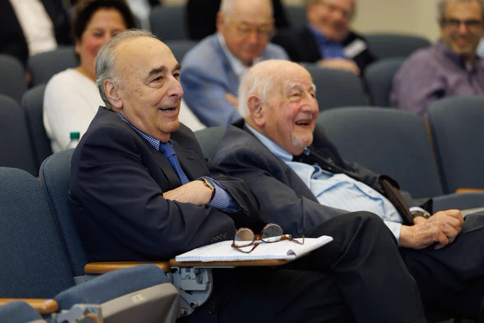 Two audience members seated in a lecture hall smile and react to a speaker during a UConn School of Law program.