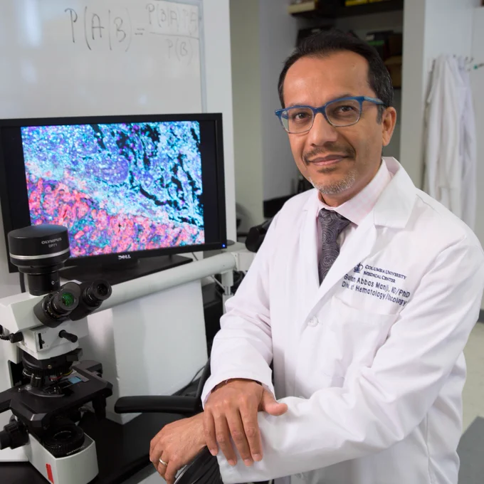 Columbia University Oncologist Gulam Manji in front of a screen showing a scientific rendering.