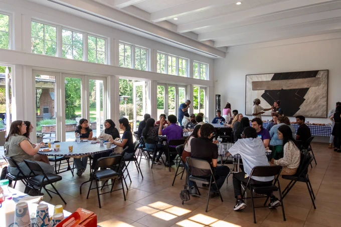 People eating at round tables in banquet room with large windows and paintings