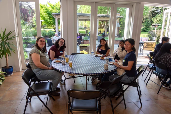 People smiling at camera around a round table in banquet hall with large glass doors