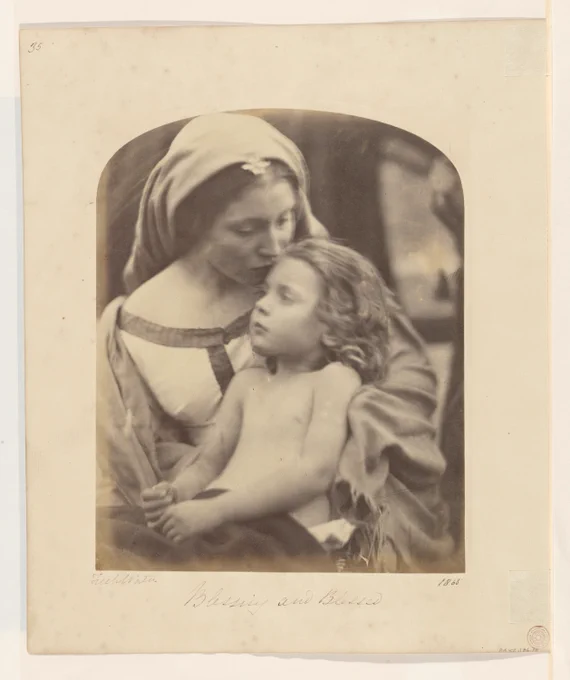 A young woman dressed in a cloak holds a child in her arms while kissing their forehead.