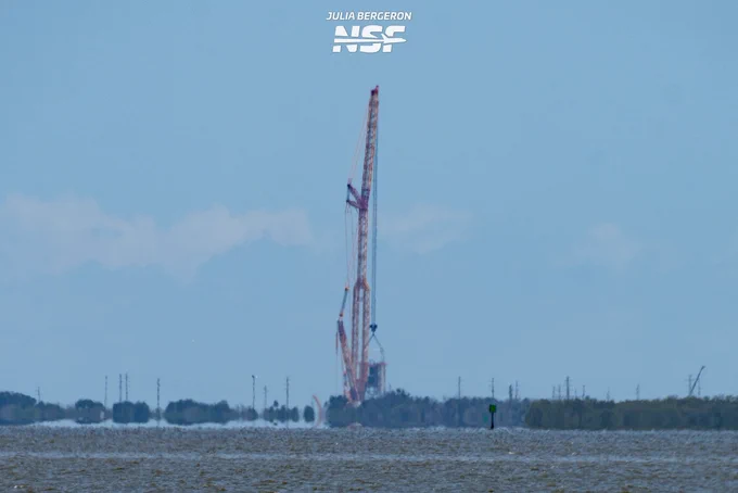 Une grue soulève un élément de la tour, le ciel bleu en arrière plan.