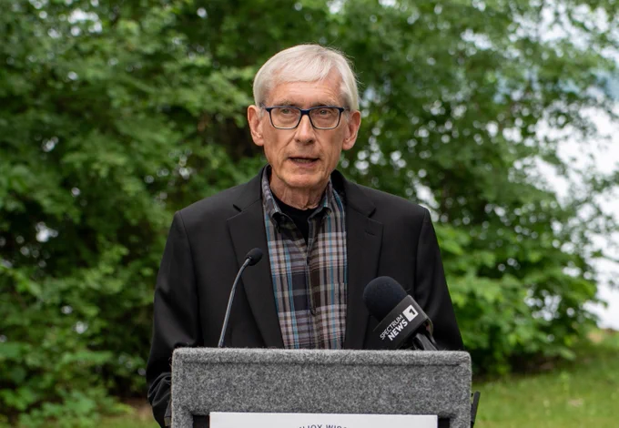 Governor Tony Evers speaking at podium with trees in background