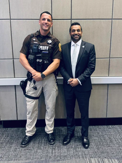 Deputy in uniform standing next to FBI director Kash Patel in a black and white suit.