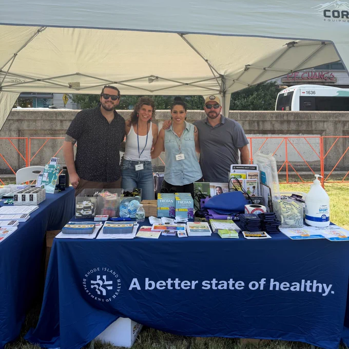 Four RIDOH staff post for a photo behind a resource table under a small pop up tent.