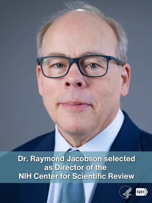 A person wearing glasses and a suit is in front of a blue-gray background. A banner at the bottom reads, "Dr. Raymond Jacobson selected as Director of the NIH Center for Scientific Review." The NIH logo is in the bottom right corner.