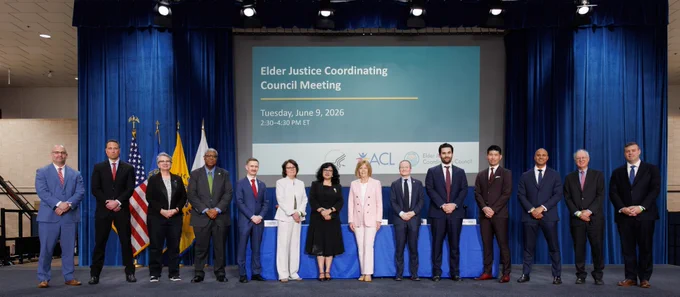 14 people stand on stage in front of a presentation screen displaying “Elder Justice Coordinating Council Meeting,” with ACL Principal Deputy Administrator Mary Lazare in the center. 