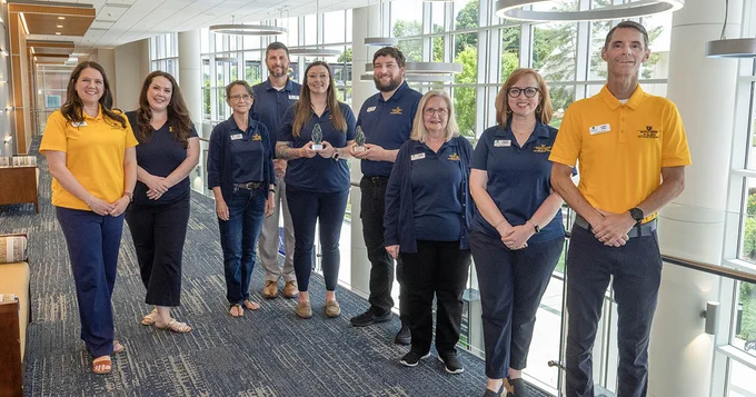 Martin Center staff pose on the second-floor balcony outside the Grand Hall, with two individuals holding the Pinnacle Awards the Center received.
