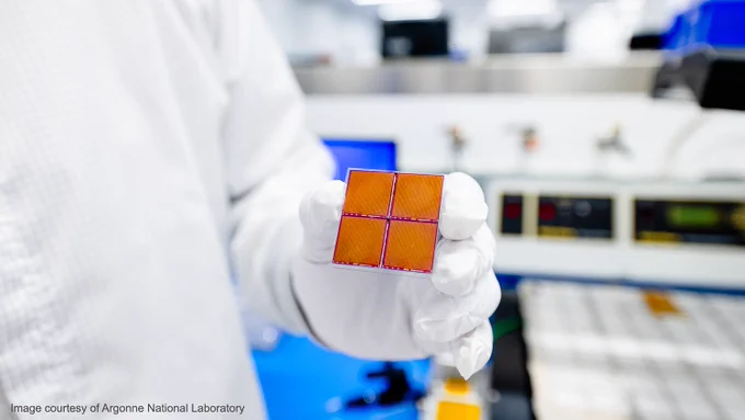 A person in a white jacket and gloves holds an AstroPix chip, which is a two-by-two square of what looks like copper-colored computer chips. Only a portion of their torso is visible. Behind them, out of focus, is laboratory equipment. The image is watermarked “Image courtesy of Argonne National Laboratory.”