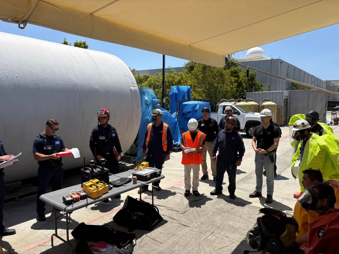 Huntington Beach firefighters assigned to the Hazardous Materials Team provide instruction to facility personnel during a training exercise. Specialized detection equipment and protective suits are displayed as participants discuss hazardous materials response plans.