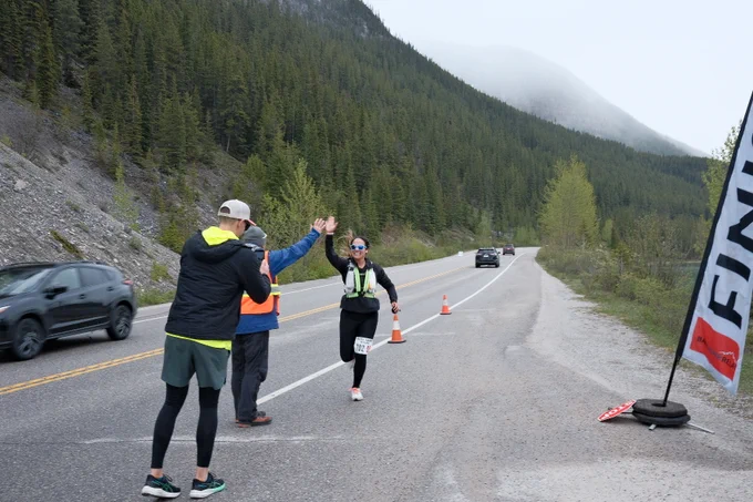 Une personne portant des lunettes de soleil et un dossard qui tape dans la main d’un supporter près de la ligne d’arrivée sur une route de montagne. 