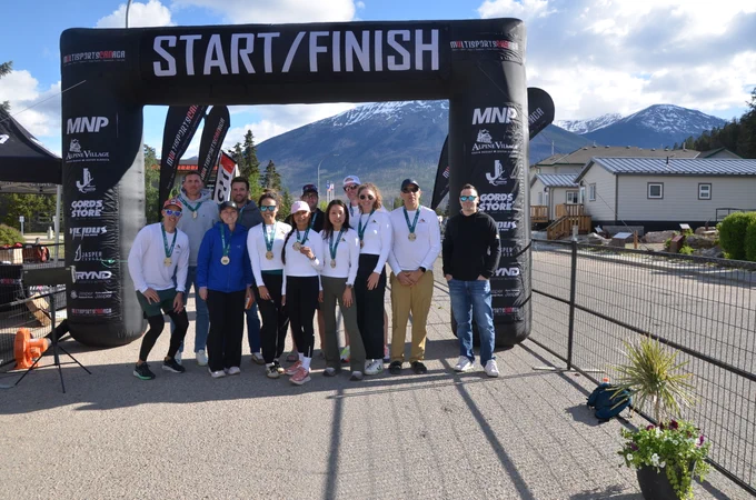 Un groupe de coureurs posant avec leurs médailles sous une arche gonflable de départ et d’arrivée lors d’une course en plein air, avec des montagnes en arrière-plan.