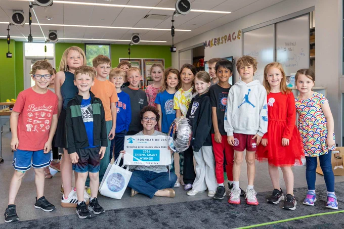 A group of children and a teacher celebrate a grant win in a classroom, showcasing a joyful and educational atmosphere.