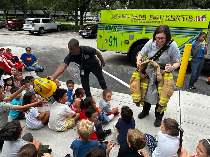 MDFR Community Affairs members pass around a helmet and bunker gear to students seated on the ground.