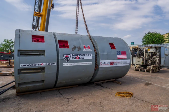 Large cylindrical tunnel boring machine labeled Midwest Mole resting on a concrete surface with a crane hook above it.